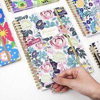Agenda hebdomadaire 2026 personnalisé avec logo, couverture florale, spirale dorée, couverture rigide avec fermeture élastique et protège-coins