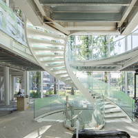 Escalier courbé durable avec structure en acier au carbone et rampes en panneaux de verre pour usage commercial intérieur