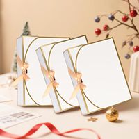 Élégante boîte cadeau pliable en kraft blanc avec dorure à chaud et nœud en ruban beige, idéale pour l'emballage de cadeaux de mariage et d'anniversaire