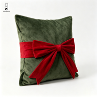 Coussin carré décoratif en velours vert foncé avec nœud rouge, idéal pour les fêtes de Noël et l'ambiance festive à la maison