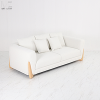 Canapé d'intérieur moderne avec accoudoirs arrondis rembourrés en blanc, pieds décoratifs en bois et coussins décoratifs pour salon