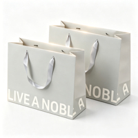 Sac cadeau en papier blanc minimaliste OEM/ODM avec poignées en ruban et typographie noire audacieuse pour la promotion d'emballages de marques de luxe modernes