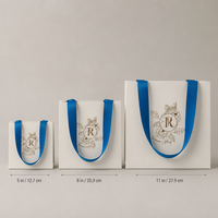 Sac en papier personnalisé avec emblème floral mat ivoire estampé à chaud or, avec poignée en ruban de satin bleu, pour cadeaux cosmétiques
