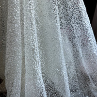 Tissu blanc opaque et scintillant avec des paillettes dorées, idéal pour les séances photo de robes de mariée et de soirée.