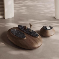 Table basse sculpturale irrégulière avec structure en bois massif et plateau en dalle de pierre, style Wabi-Sabi, inspirée des galets, conçue par des designers pour les villas.