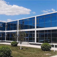 Grande structure de bureau modulaire préfabriquée en conteneurs en forme de L sur deux étages, avec façade en verre bleu, fenêtres à auvent, maison mobile et portable