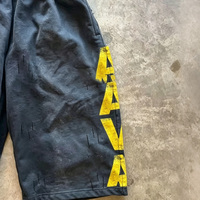 Shorts en molleton noir délavé vintage pour homme, avec imprimé lettres jaunes sur le côté, style streetwear usé, longueur genou