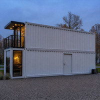 Maison préfabriquée à deux étages avec façade vitrée ouverte et terrasse de jardin