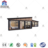 Maison préfabriquée en conteneur extensible en forme de L, résistante aux intempéries, avec finition en bois foncé et fenêtres du sol au plafond