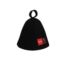 Un gorro de sauna negro de pura lana que hereda el legado en su frente mientras el calor rinde homenaje a los setenta y cinco años de maestría.