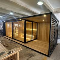 Sauna extérieur moderne avec douche de pluie intégrée, plateforme en bois, cadre noir, porte en verre, chauffage en pierre pour jardin et cour arrière