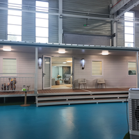 Maison modulaire préfabriquée moderne avec large porche couvert, balustrade et porte d'entrée en verre pour chambre d'amis dans la cour