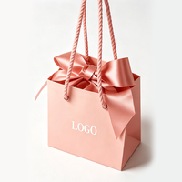 Sac en papier cadeau de luxe rose personnalisé avec logo et nœud en soie, idéal pour l'emballage de vêtements et de parfums, parfait pour les cadeaux de mariage et d'anniversaire.