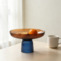 Twee-kleurige glazen fruitschaal, amberkleurige plaat met blauwe geribbelde voet, moderne decoratieve serveerschaal op voet voor thuis op tafel.