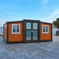 Maison conteneur pliable extensible bleu foncé à bardage horizontal avec portes et fenêtres latérales en verre pour le glamping en bord de lac