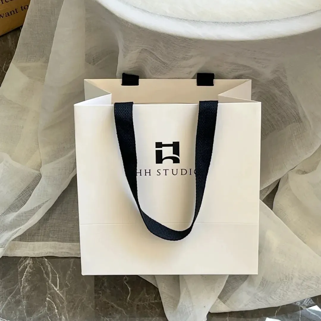 Bolsas de regalo de papel blanco al por mayor, bolsa con asa de papel ecológica a granel, bolsa de papel de moda personalizada con su propio logotipo