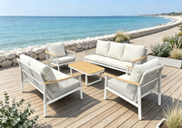 Ensemble de salon d'extérieur moderne en métal blanc, sièges à texture tressée, tables rondes avec accents en bois et coussins gris moelleux, idéal pour le patio