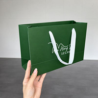 Sac cadeau en papier vert forêt de luxe avec logo blanc minimaliste et poignées en ruban doux pour l'emballage de produits de soin et de cosmétiques