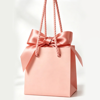 Sac en papier cadeau de luxe rose personnalisé avec logo et nœud en soie, idéal pour l'emballage de vêtements et de parfums, parfait pour les cadeaux de mariage et d'anniversaire.