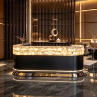 Comptoir de réception en pierre naturelle rétroéclairée, quartz blanc cristallin, translucide et lumineux, avec base noire mate et finition métallique.