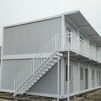 Maison conteneur démontable, revêtement bleu marine, structure blanche, deux étages avec balcon et escalier extérieur, pour usage bureautique ou en parc.