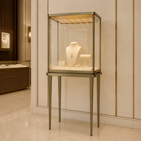 Vitrine de présentation de bijoux élégante, en verre transparent, avec cadre en métal doré, pieds hauts et éclairage LED pour les bijouteries de luxe