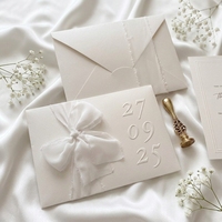 Carte de vœux de luxe en papier de coton texturé blanc avec monogramme en relief, manchon en mousseline avec nœud, double bordure, impression typographique personnalisée