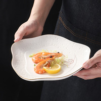 Assiette en céramique de luxe à bord doré avec surface texturée en relief, forme carrée irrégulière pour la restauration fine et les événements