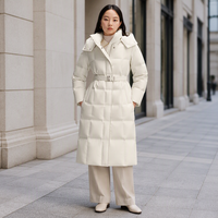 Vente en gros de manteaux longs en duvet pour femmes, couleur beige, avec ceinture, capuche en fausse fourrure, veste matelassée
