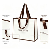 Sac cadeau en papier blanc personnalisé avec bordure marron, poignée en ruban satiné, logo de marque imprimé pour boutique de vêtements, emballage cadeau de luxe