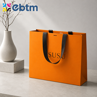 Sacs cadeaux en papier orange de luxe personnalisés en gros avec poignées en ruban noir pour l'emballage de détail