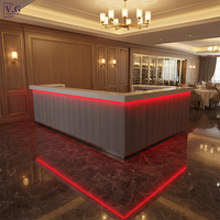 Comptoir de bar moderne en forme de L avec dessus en Corian blanc et façade gris foncé, éclairage LED RGB sous le comptoir, personnalisable pour restaurant/hôtel/club