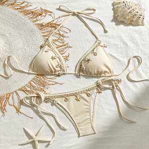 Bikini de mujer con parte inferior de tanga acanalada, ribete de encaje y dijes de concha, color beige. - Product Image 1