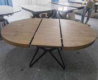 Table à manger extensible de style italien, dotée d'un plateau circulaire à grain de bois riche et d'une base croisée en métal noir aux lignes épurées.