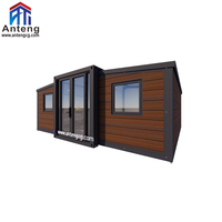 Maison conteneur pliable extensible en bois foncé avec toit à pignon et terrasse, spacieuse et privée, pour famille ou invités