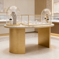 Table de présentation de bijoux de luxe avec plateau en marbre et pieds cylindriques en or brossé |   Vitrines en verre éclairées par LED avec socles en forme de dôme |   Personnalisable