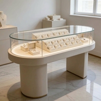 Moderner Cremeweißer Ovaler Schmuck-Präsentationstisch LED-Beleuchtete Glasvitrine für Einzelhandels-Schmuckgeschäfte