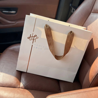 Sacs shopping personnalisés en carton blanc avec logo gaufré, pelliculage mat et poignées en corde chevronnée marron pour marques de vêtements
