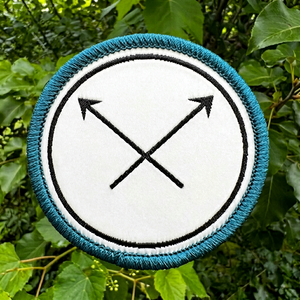 Parche bordado circular con diseño de flechas cruzadas y ribete azul, insignia para coser en ropa y decoración. - Product Image 1