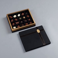 Boîte à bonbons et chocolats en carton rigide avec insert en plastique, ornée de nœuds en ruban à bord doré, pré-noués, en satin élastique, et de décorations.