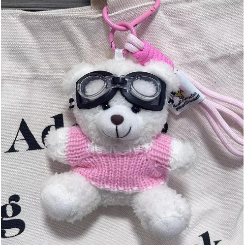 Un ours blanc avec des lunettes, des vêtements roses et une corde suspendue rose.