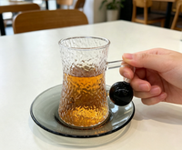 Ensemble de tasses à café en verre borosilicate martelé à forme cintrée, avec poignée boule noire, forme sablier texturée, et soucoupe gris fumé classique pour le thé