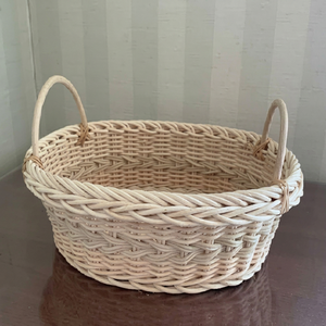 Cesta ovalada de mimbre de color claro, tejida con un borde grueso trenzado y asas altas y arqueadas que salen del centro. - Product Image 1