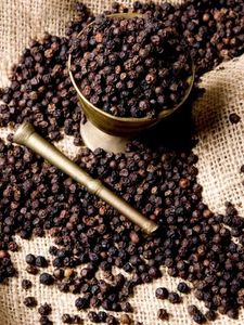 Granos de pimienta negra en cuchara de madera sobre fondo negro para condimentar en la cocina - Product Image 1