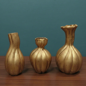 Siluetas de jarrones de metal dorado inspirados en calabazas orgánicas: una suave curva asimétrica, una forma de reloj de arena voluminosa y un cuello estriado alargado. - Product Image 1