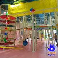 Structure de grimpette intérieure multi-niveaux en filet blanc avec poteaux rembourrés et plateformes colorées – Équipement commercial pour centre de jeux pour enfants