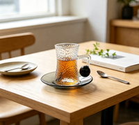 Ensemble de tasses à café en verre borosilicate martelé à forme cintrée, avec poignée boule noire, forme sablier texturée, et soucoupe gris fumé classique pour le thé