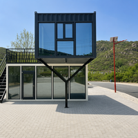 Maison préfabriquée contemporaine en conteneur à deux étages, avec toit en pente imitation bois, mur entièrement vitré et design cantilever.
