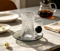 Ensemble de tasses à café en verre borosilicate martelé à forme cintrée, avec poignée boule noire, forme sablier texturée, et soucoupe gris fumé classique pour le thé