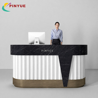 Bureau d'accueil de luxe en marbre noir avec panneaux cannelés blancs, base en bronze, détail avant conique et design moderne pour hall d'entreprise